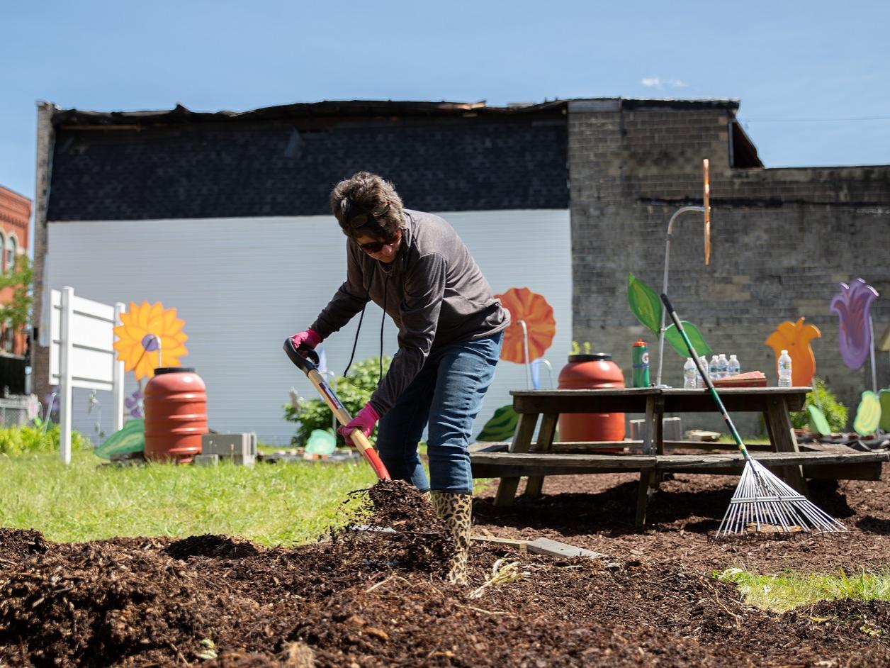 Woman shovels mulch at community garden