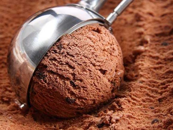 A tub of chocolate ice cream and a silver scooper.