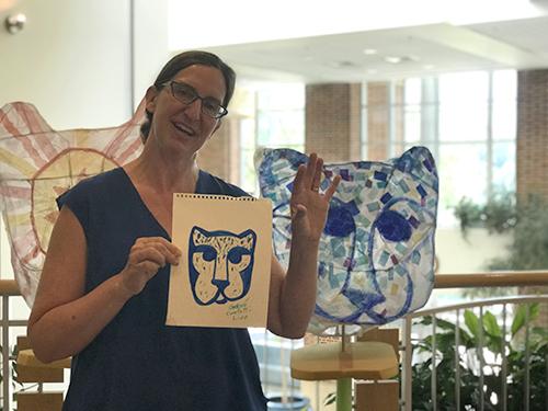 Cheryl Capezzuti holding a drawing in front of a puppet modeled on the Nittany Lion
