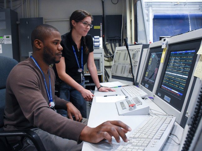 Two nuclear engineering students lean over computers in the control room at the Breazeale Nuclear Reactor on Penn State's campus. 
