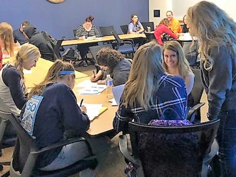 A group of students in a large classroom discussing their classroom project.