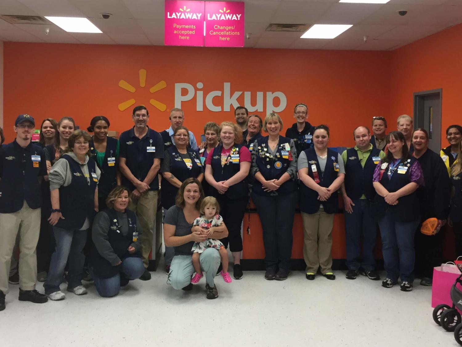 A group of people in Wal-Mart vests pose for a photo with a woman and her young daughter.