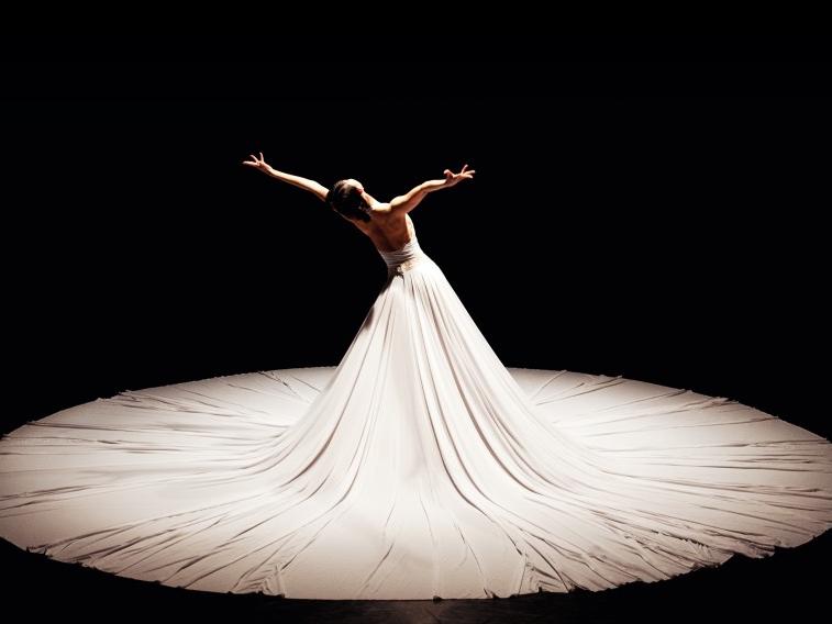A dancer wears a white gown with the skirt arranged in a circle around her.