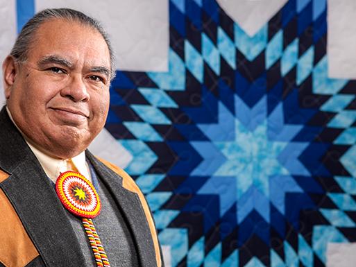 Penn State professor John Sanchez sits in front of an American Indian quilt.