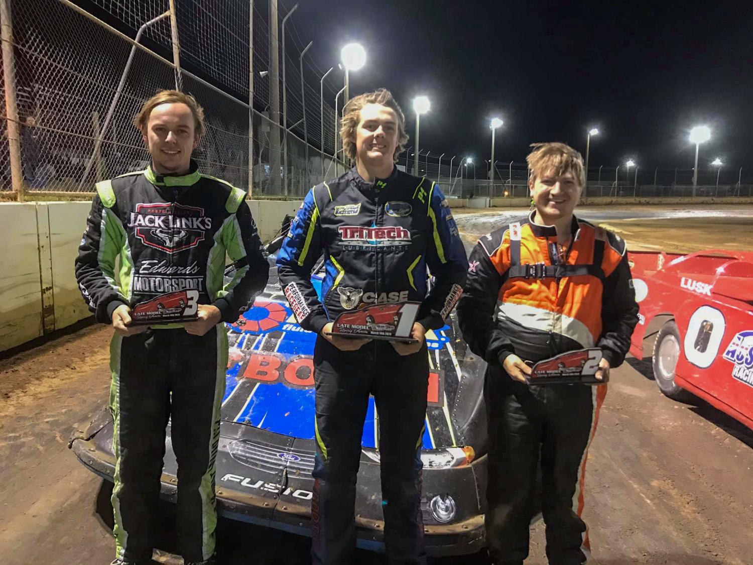 Three people in racing gear on a racing track in Australia