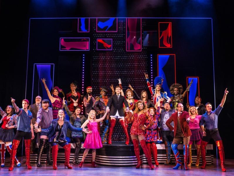 A varied cast of actors gesture with their arms during a musical number in “Kinky Boots.”