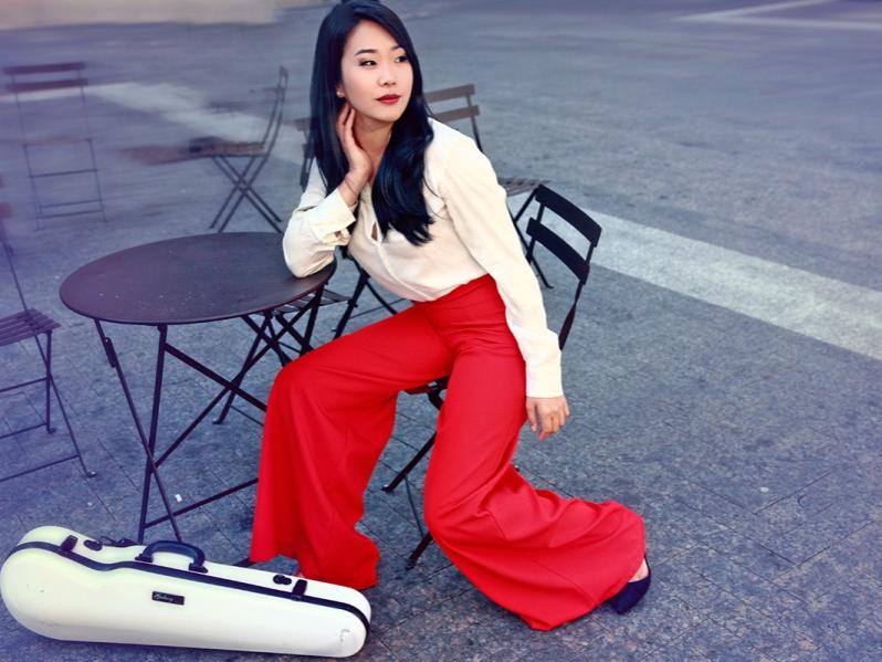 A woman sits and rests her arm on a bistro table while she looks off to her left.