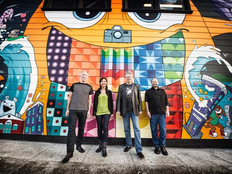 Three men and a woman stand in front of a wall covered in graffiti.
