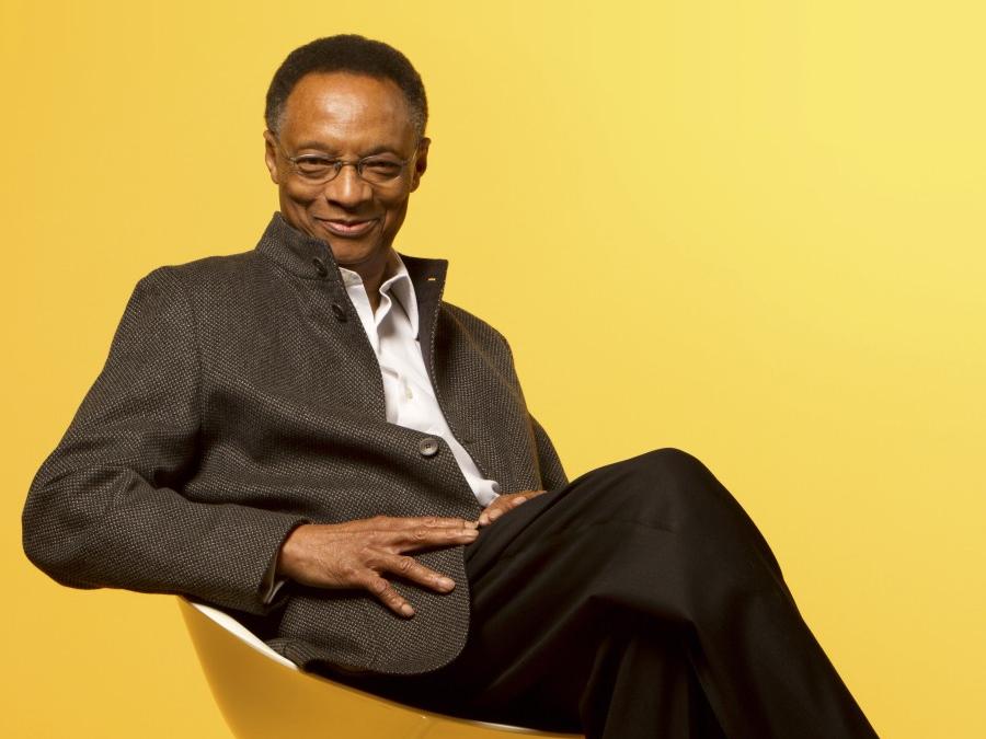 Pianist Ramsey Lewis sits with his legs crossed in a chair facing the photographer.