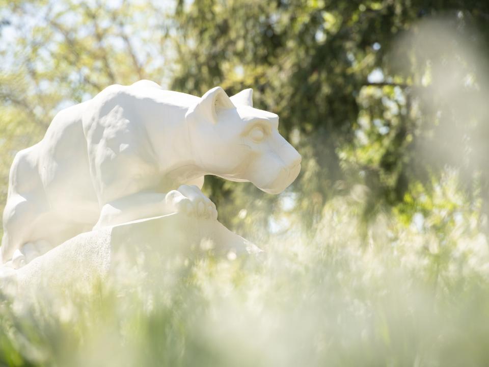 Photo of white Nittany Lion statue through out-of-focus flowers and grass nearby