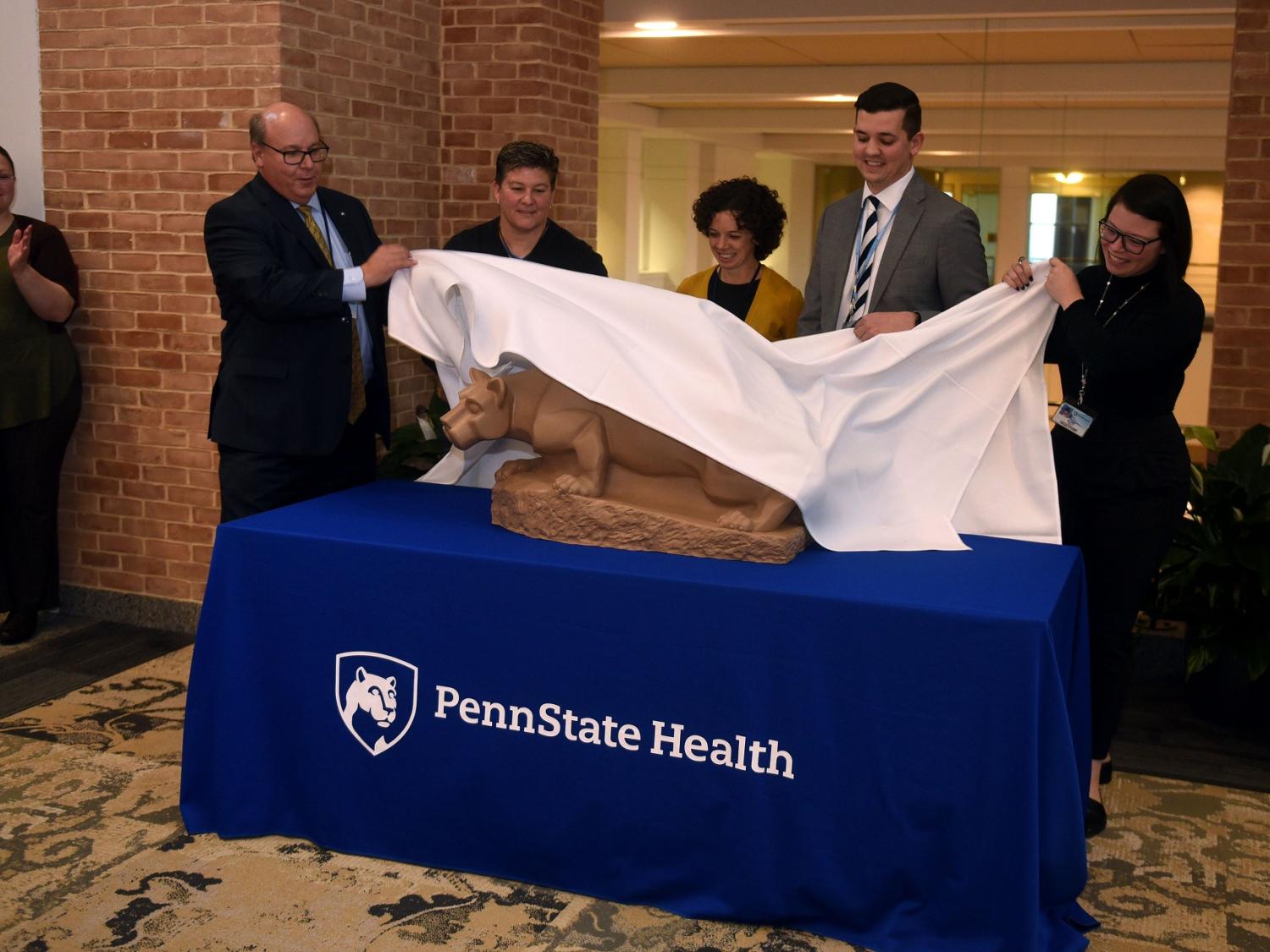 Five people take a cloth off to reveal a statue of a lion