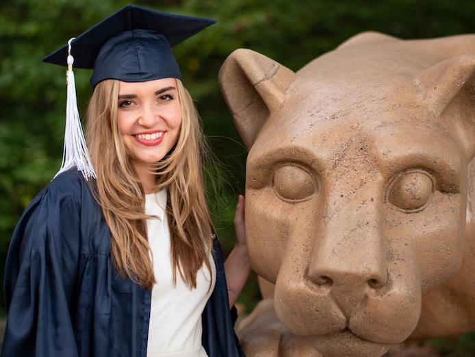 Graduate posing with Nittany Lion Shrine