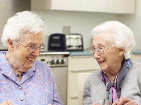 Two older women sit at a table, talking.