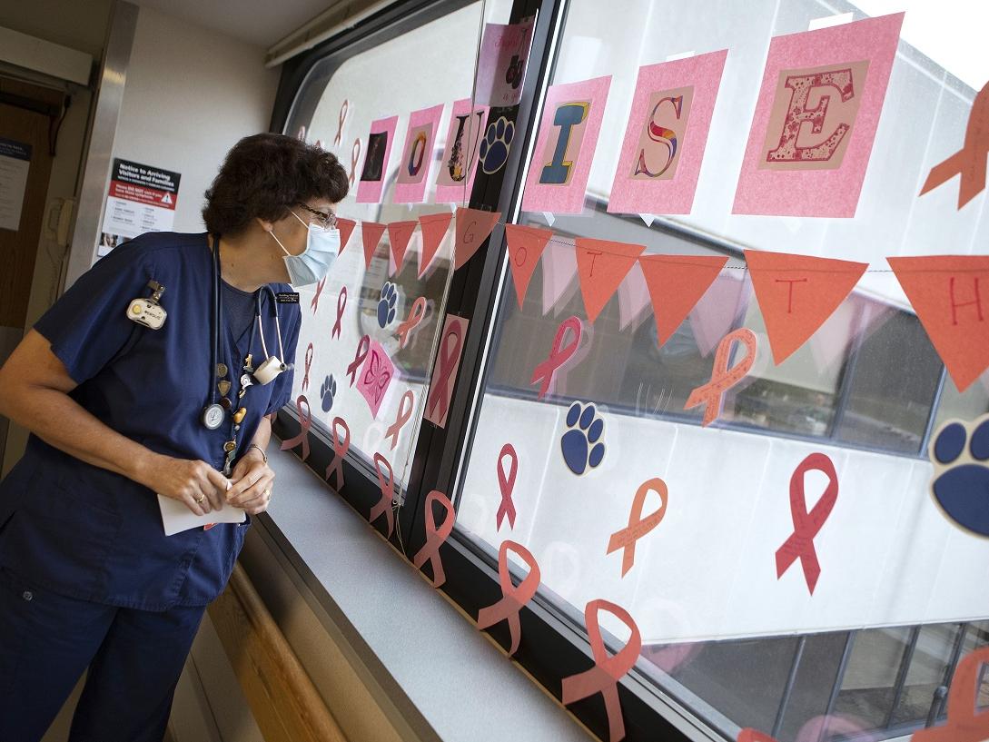 Louise Kline, wearing a mask and scrubs, examines a window upon which are construction-paper decorations. The name Louise is spelled out in big letters.