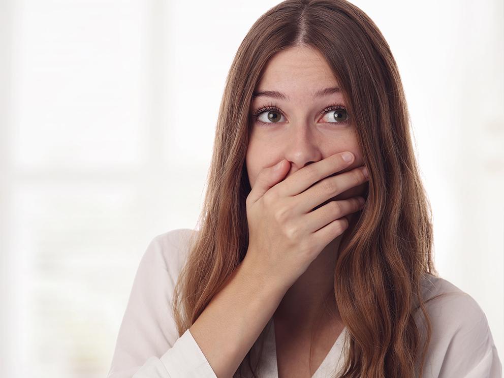 A woman holds her right hand up to cover her mouth, as her eyes look slightly upward and to the side.