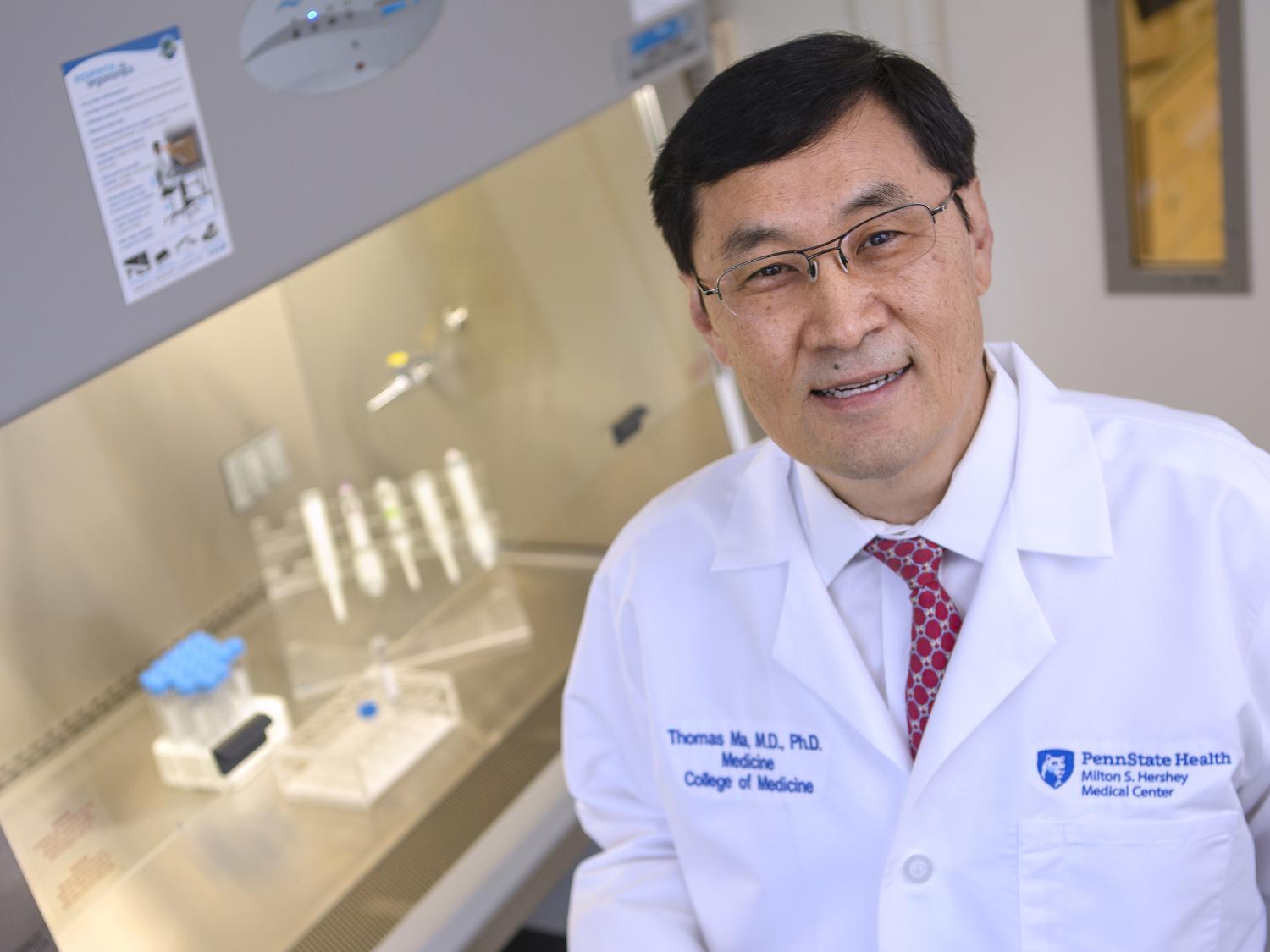 Dr. Thomas Ma poses for a photo, with a lab workbench and equipment in the background.