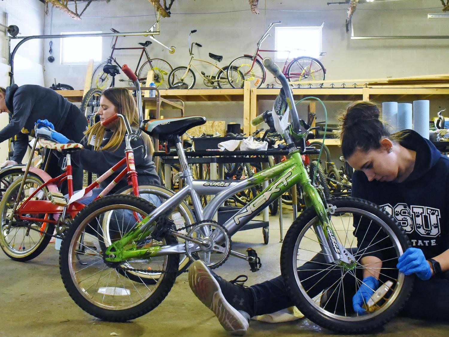 Three Penn State students repair bicycles at the Sisters of St. Joseph Neighborhood Network bike warehouse.