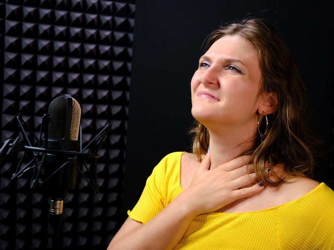 A young woman holds her throat while standing near a microphone.
