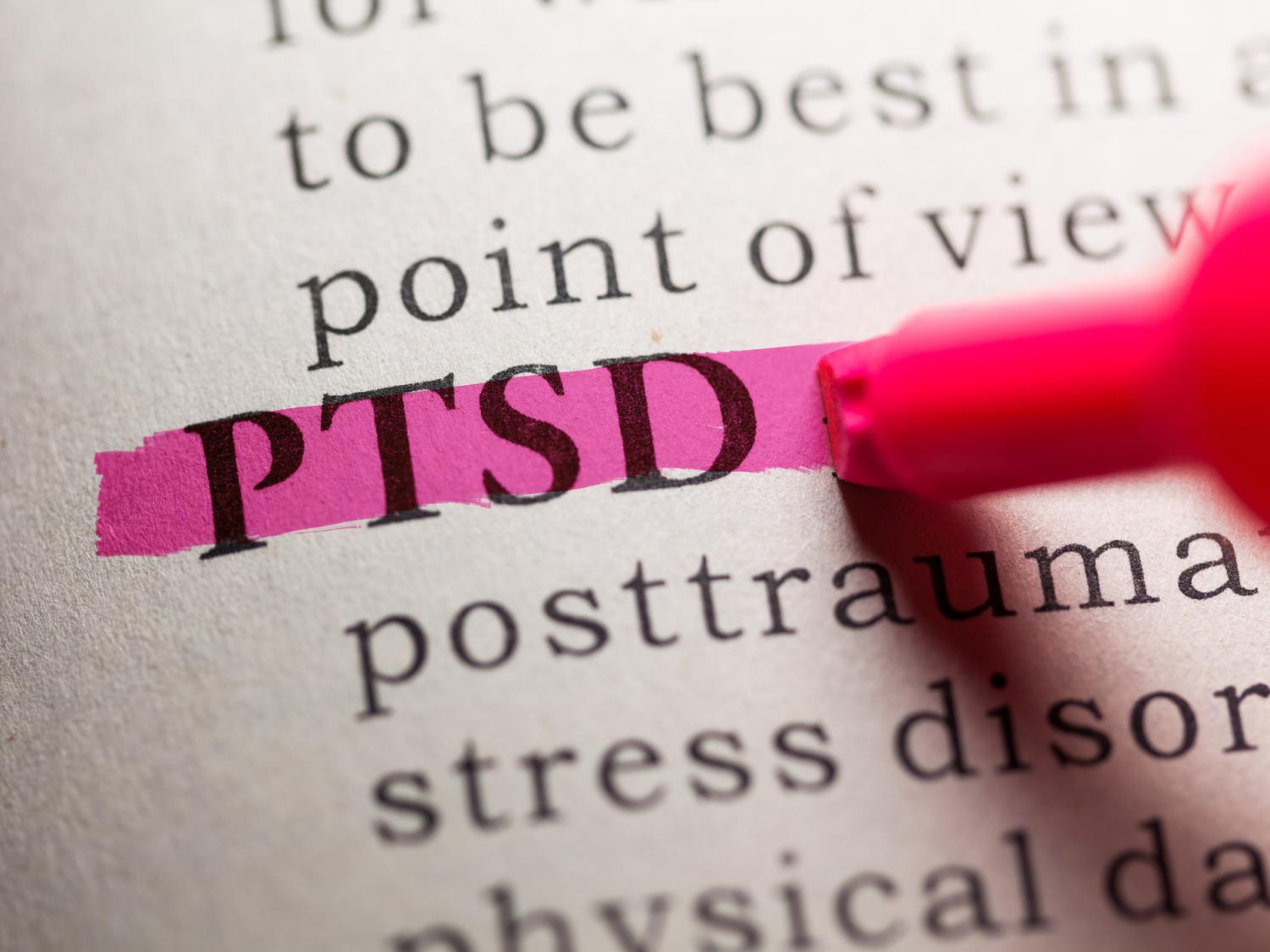 Close-up of the acronym “PTSD” in a book being highlighted by a marker.