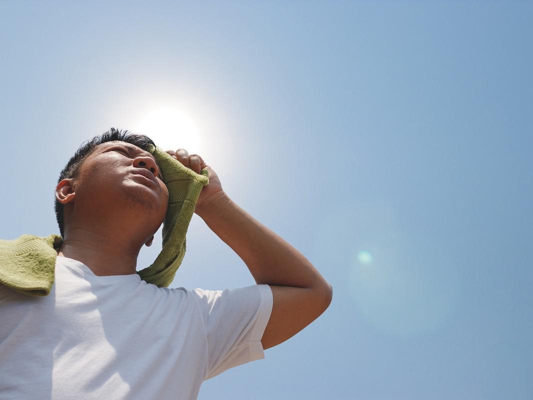 A man holds a towel to his forehead as the sun blazes overhead.
