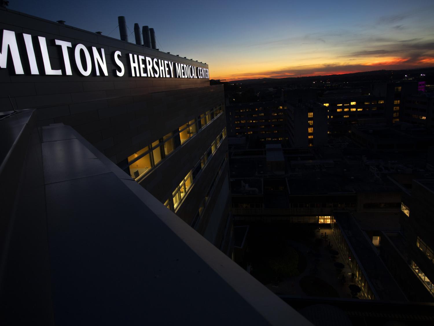 An illuminated sign reading "Milton S. Hershey Medical Center" appears on a building at dusk.