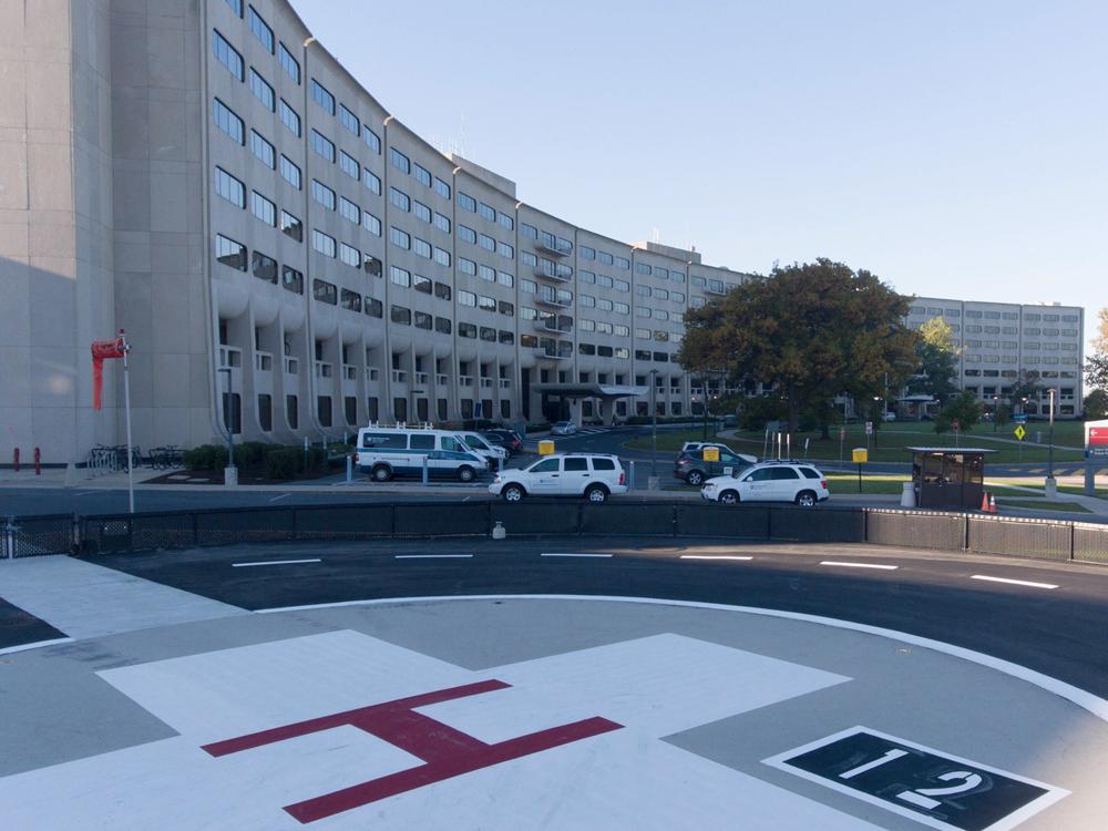 The Life Lion helipad at Hershey Medical Center is in the foreground, with a large white cross with a red "H" in the middle. The Medical Center's signature Crescent building is in the background.