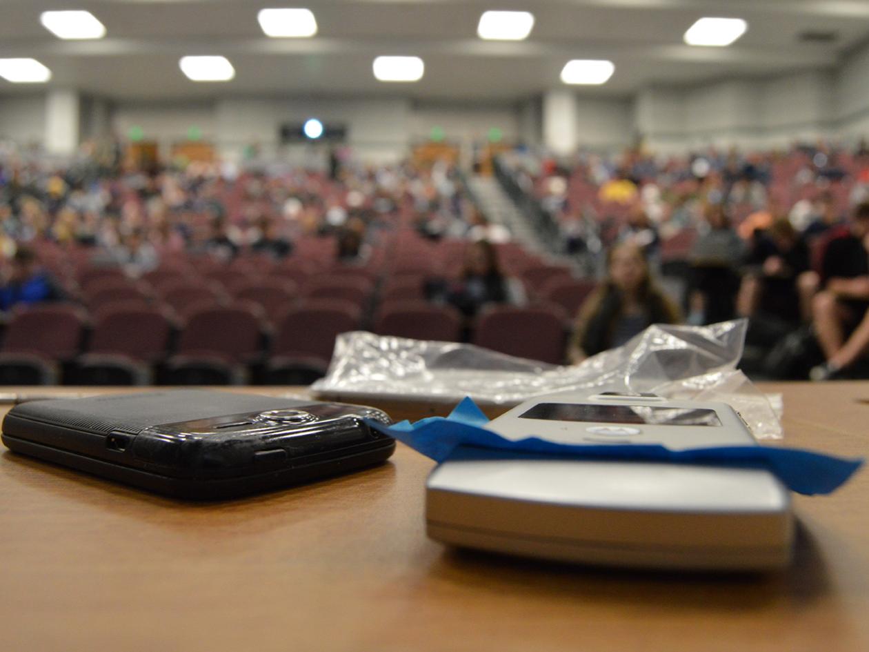 phones in foreground of classroom, with students out of focus in background