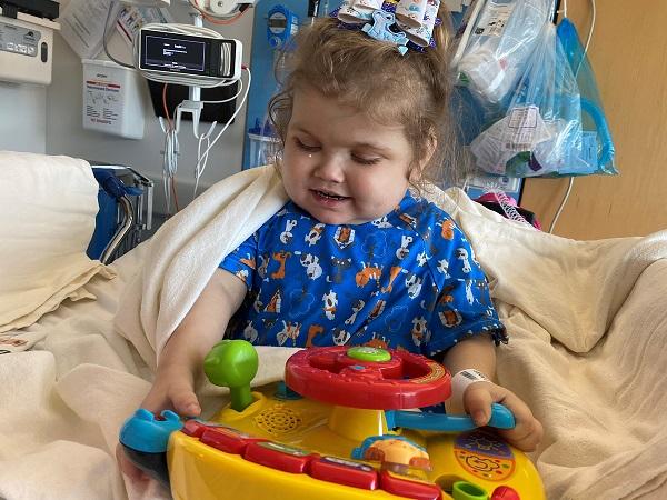 Malaya Gohn plays with a toy and smiles while sitting in a hospital bed.