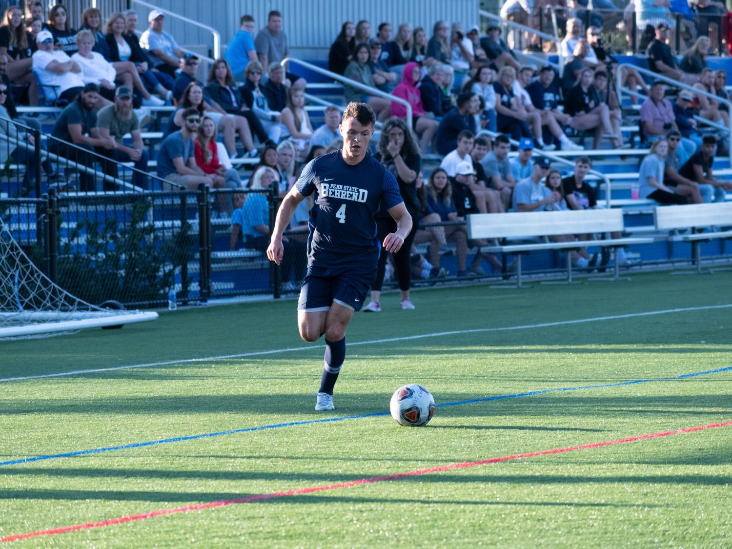 A Penn State Behrend soccer player dribbles the ball upfield.