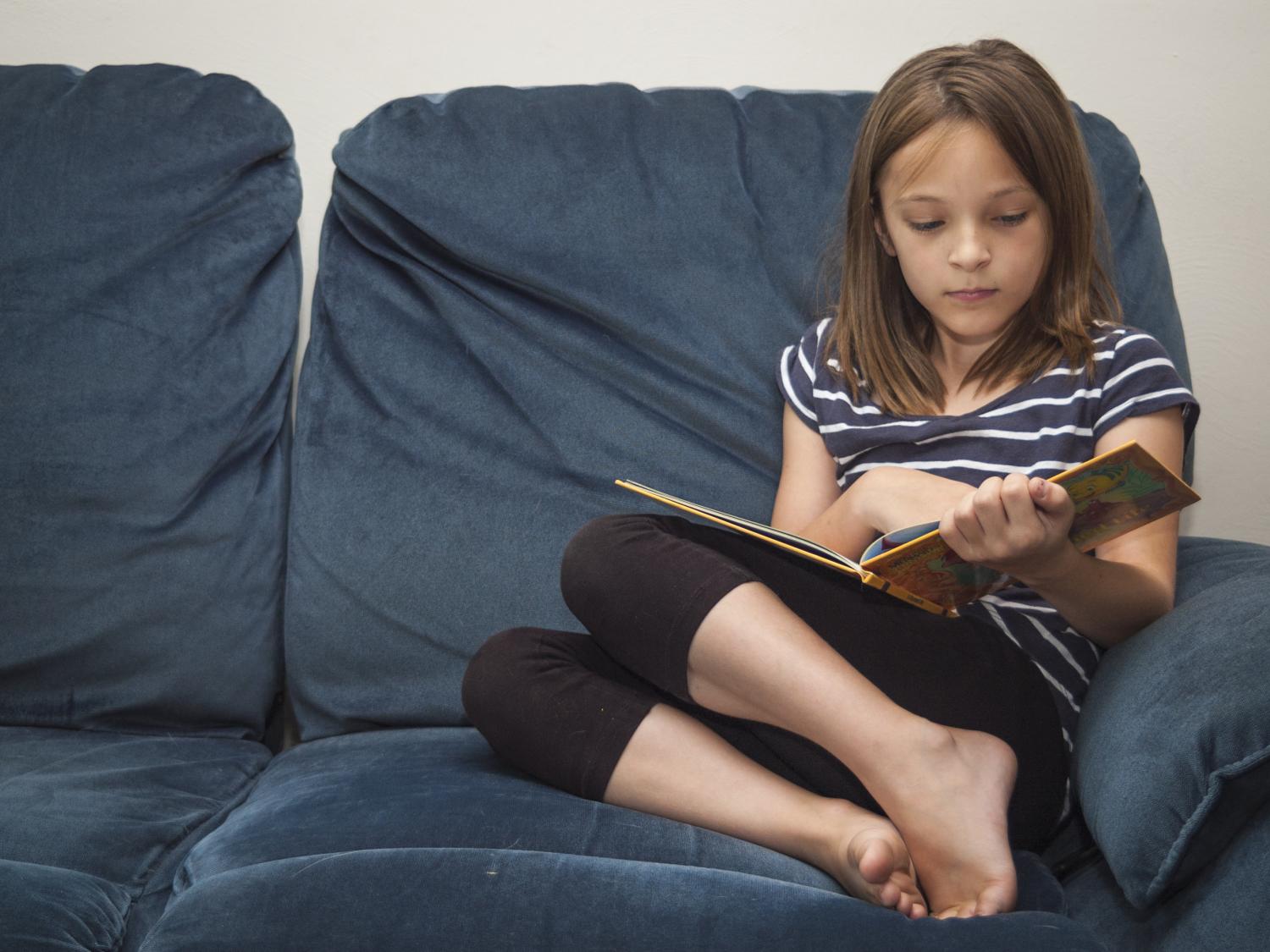 A young girl reading a book on a blue couch