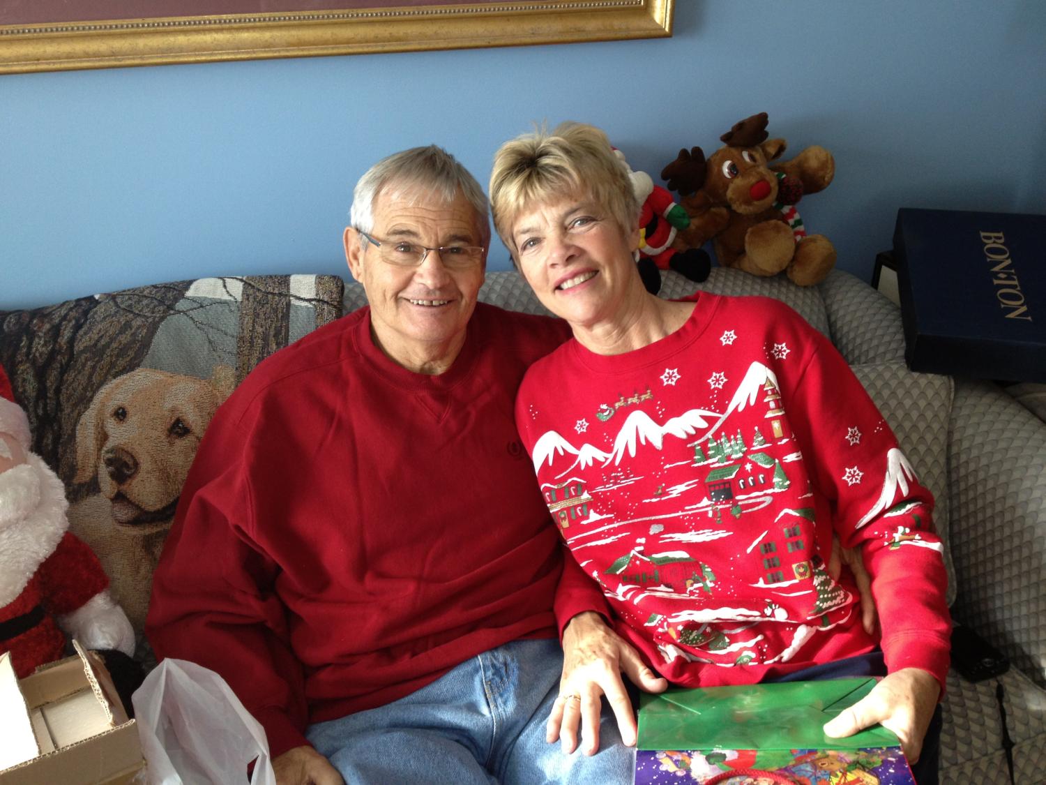 Jim Miller and his wife JudyBeth sit on a couch, posing for a photo. Both are smiling, and Jim's arm is around JudyBeth.