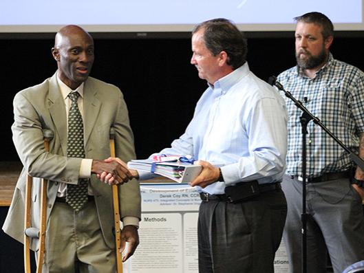 Chancellor Francis Achampong hands the WCHS project policies and procedures book to WCHS President Greg Duffey.