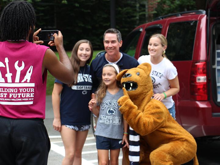 An orientation leader takes a family photo of a first year.