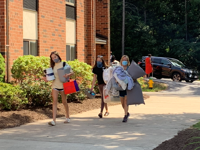 Students and a parent carrying boxes and other belongings on a sidewalk into North Hall