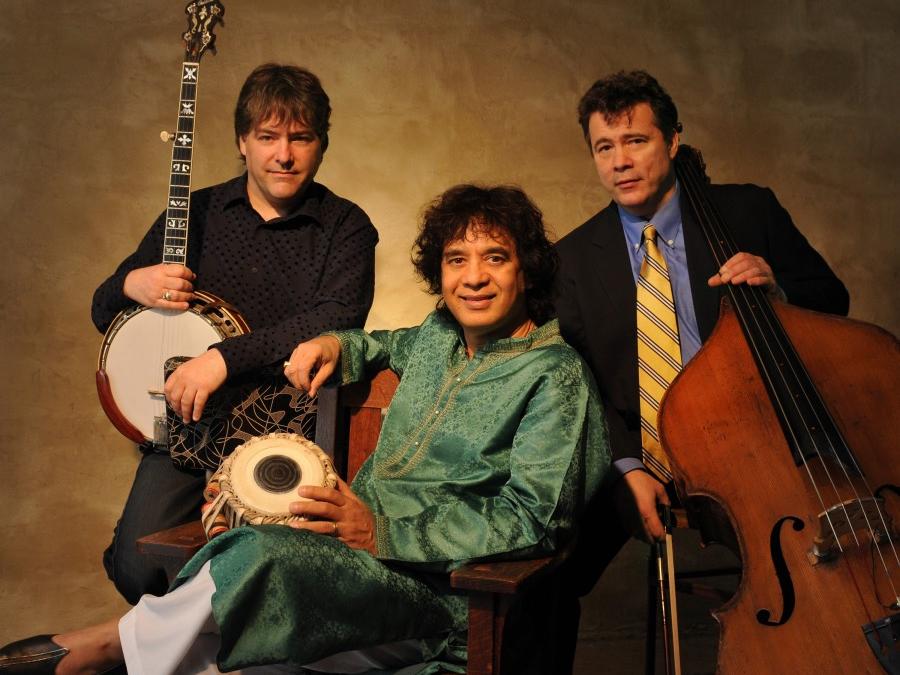 Three men sit in chairs and hold their instruments.