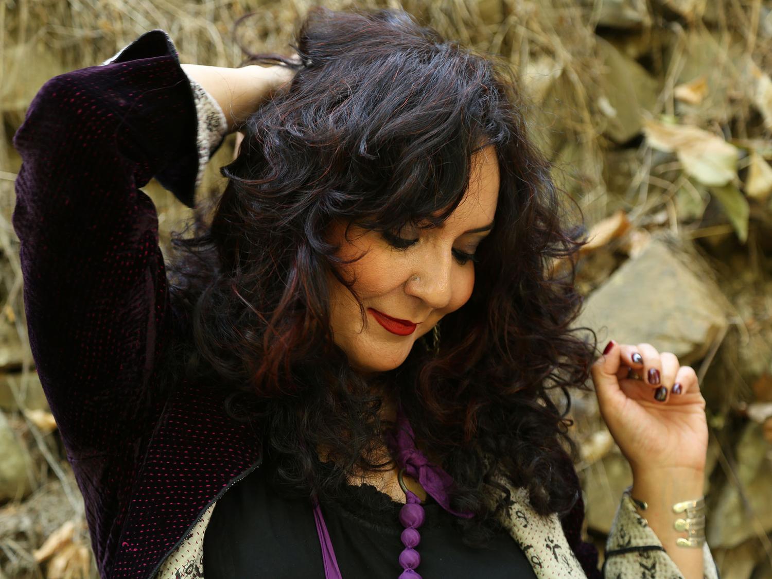 A woman smiles and holds one arm behind her head.