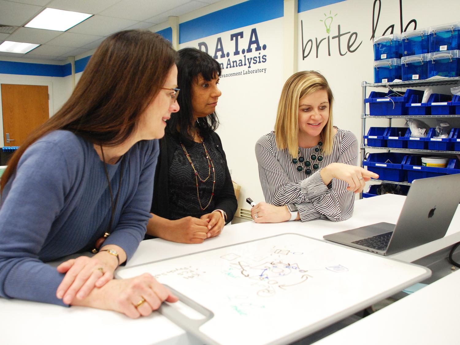 Two women looking at a computer screen as another woman points to the screen