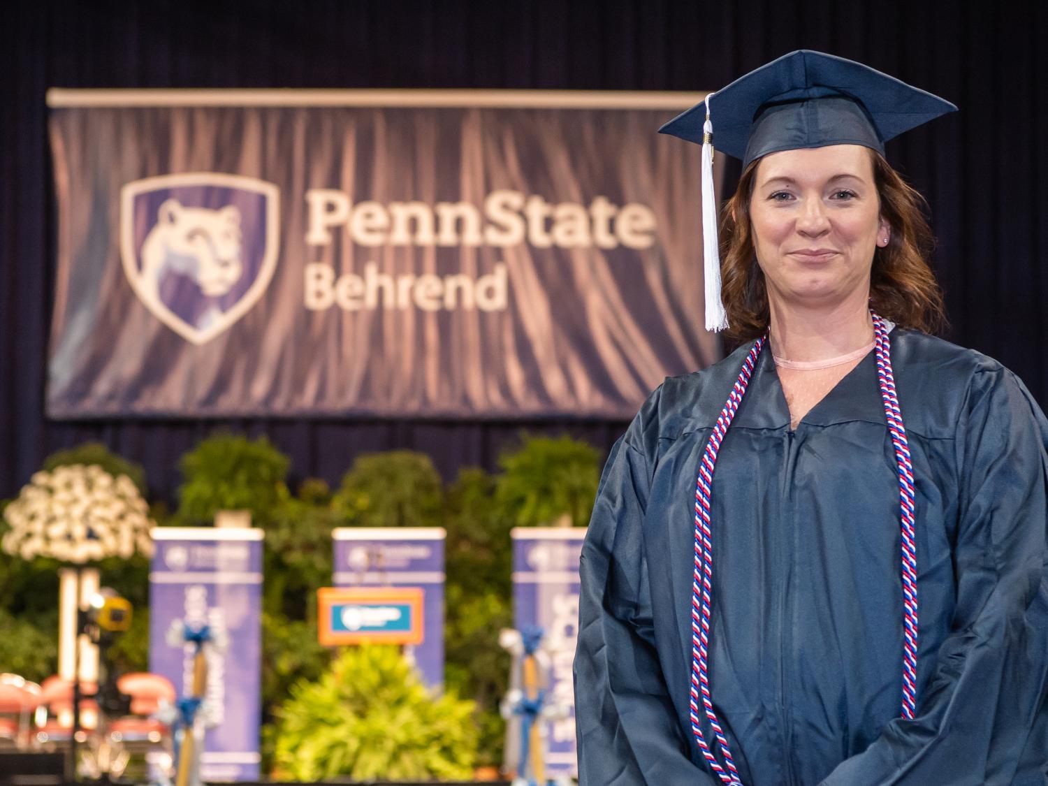 A Penn State Behrend graduate poses on the commencement stage.