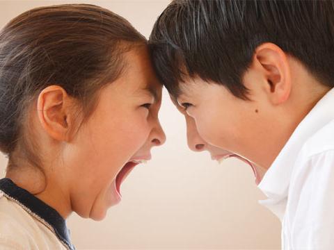 A young brother and sister with heads together yelling at each other.