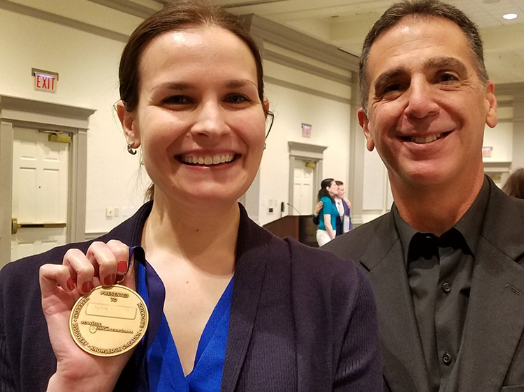 student proudly holding award medal alongside her mentor