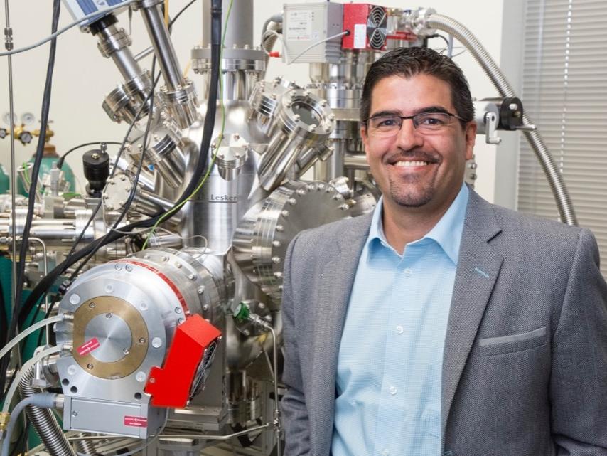 A man stands in front of a laboratory machine used in nuclear engineering research.  