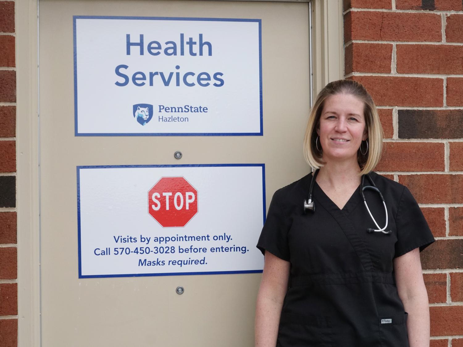 Woman in scrubs standing in front of office door with signs denoting campus health services.
