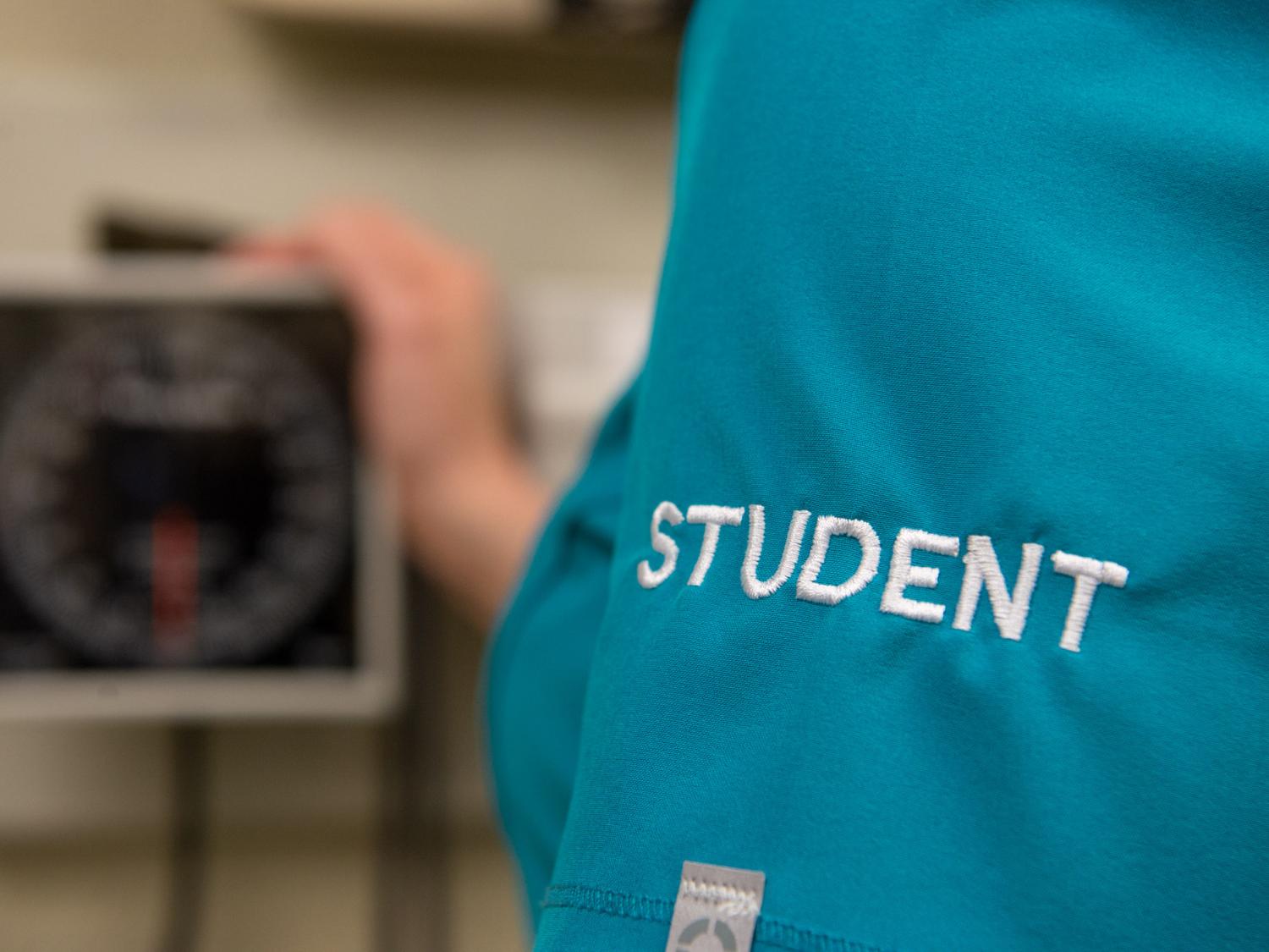 An image of a person wearing scrubs that say student on them, and a piece of medical equipment.