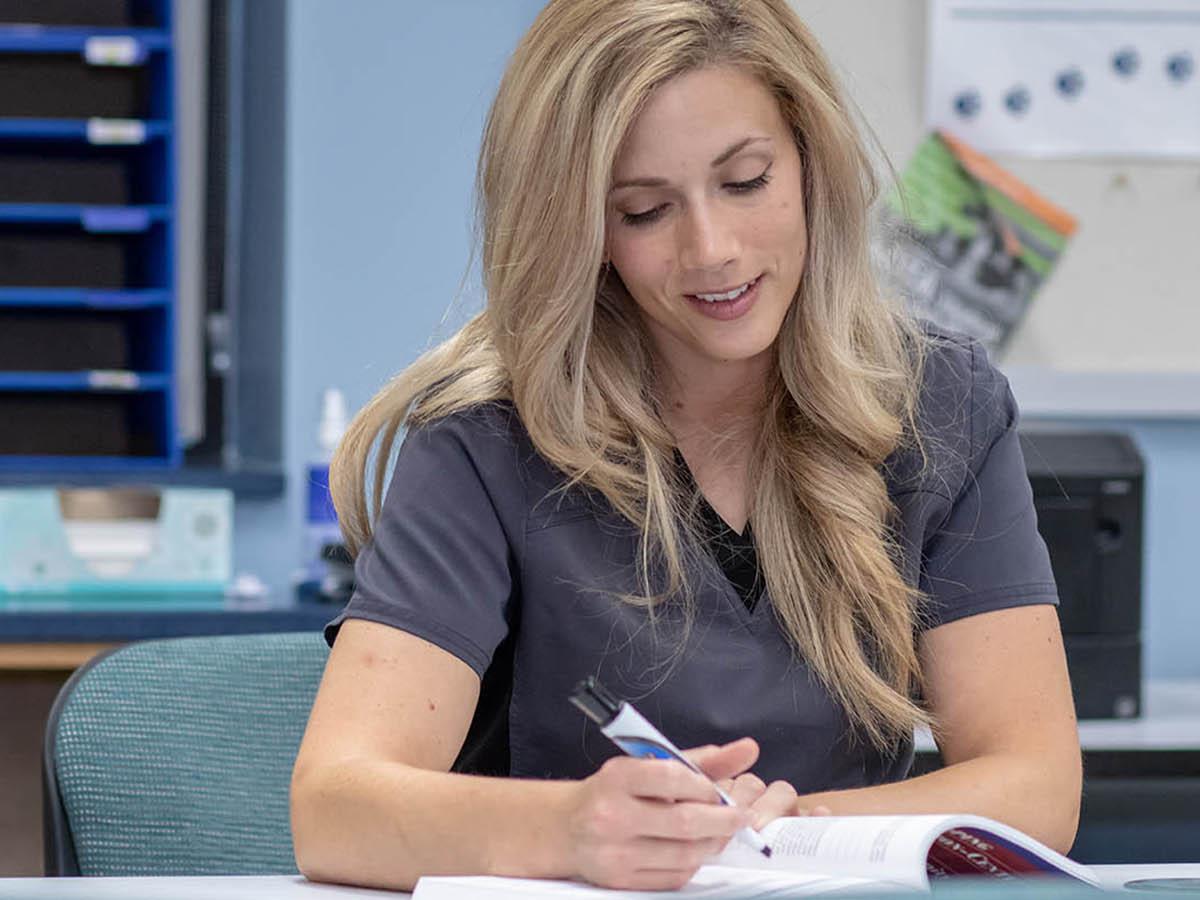 A female student is pictured completing paperwork in the campus's OTA Lab.