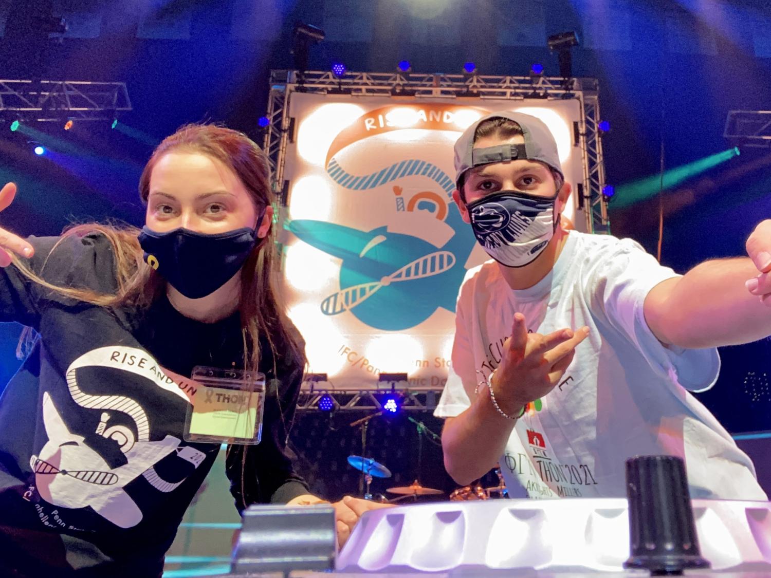 Two college students wearing masks pose for the camera on a brightly lit stage.
