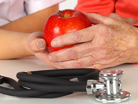 Two hands holding an apple with a stethoscope in the foreground