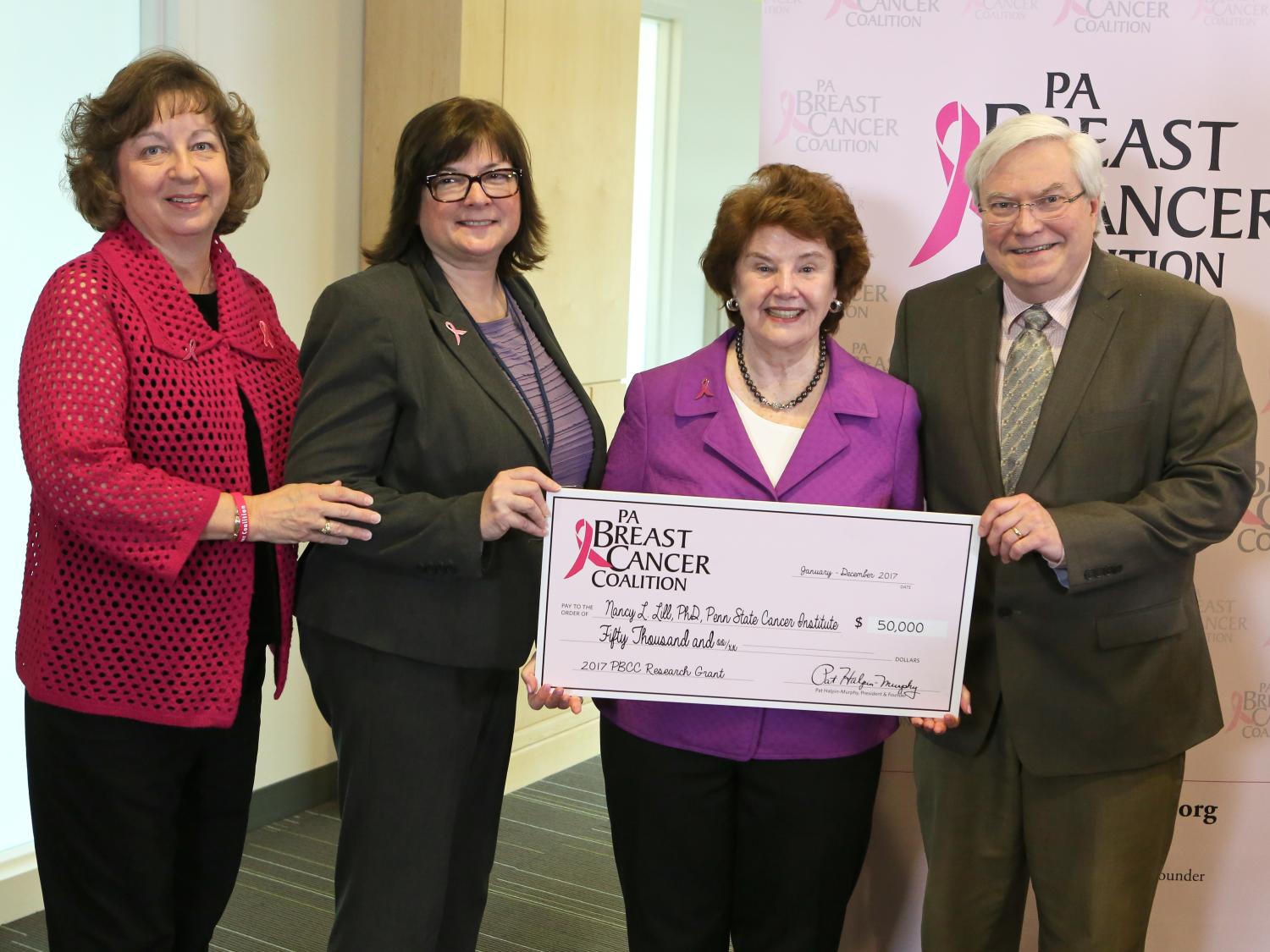Four people pose with a check in the amount of $50,000. A backdrop with the PA Breast Cancer Coalition logo is behind them.