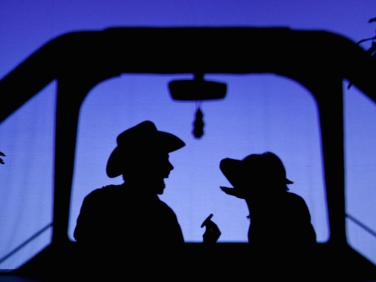 Pilobolus dancers depicting a man wearing a cowboy and a dog sit in the silhouette of a car in a scene from “Shadowland.”