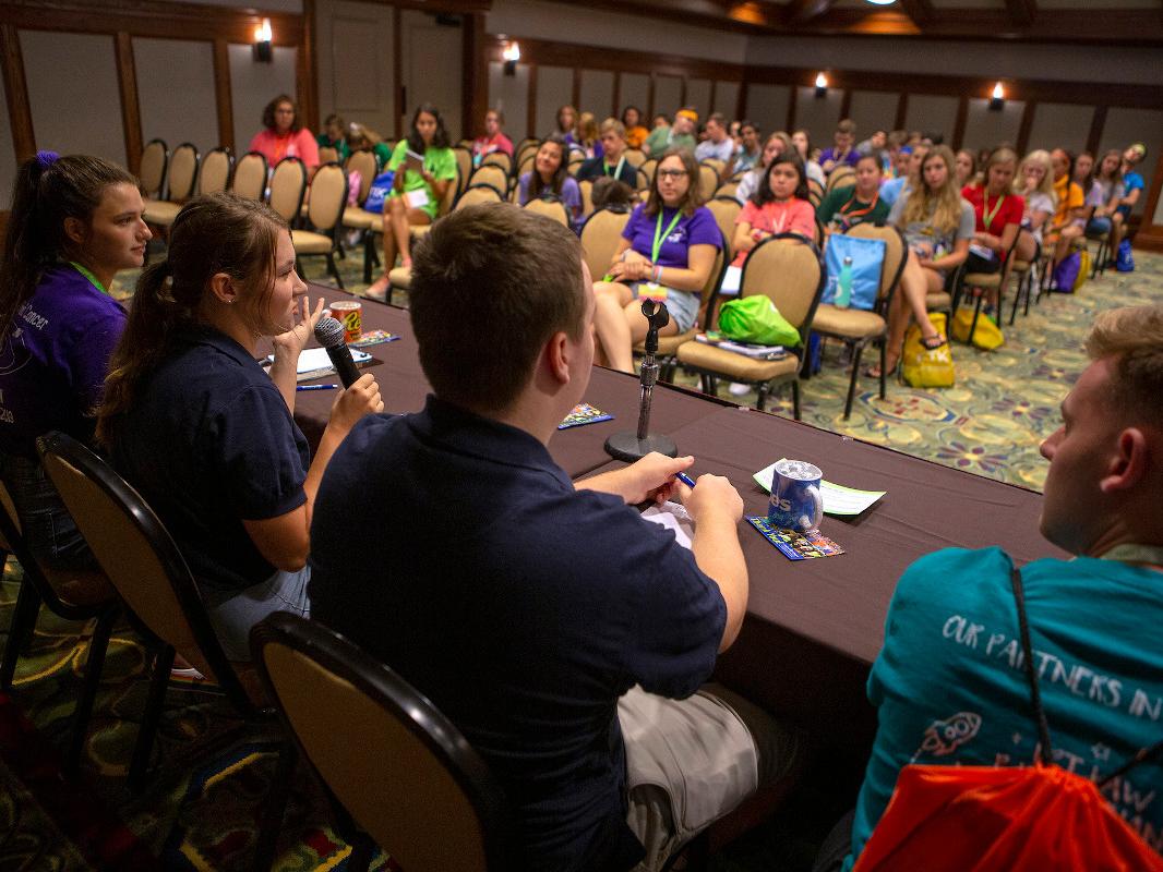 students sit in the front of a room and speak to a crowd