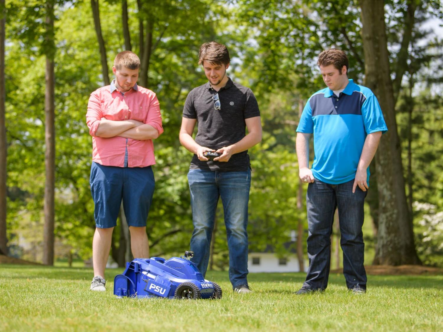 Three Penn State Behrend students test a remote-control lawn mower.